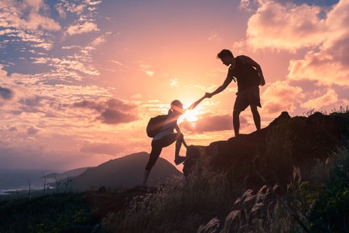 Team work, life goals and self improvement concept. Man helping his female climbing partner up a steep edge of a mountain.